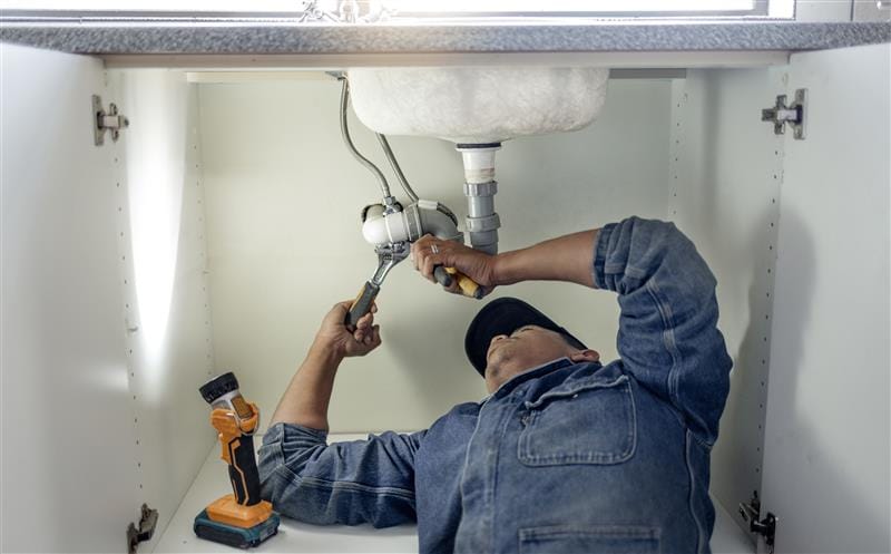 Plumber repairing pipes beneath a bathroom sink in Lebanon