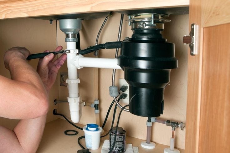 Plumber installing a garbage disposal beneath a kitchen sink in Lebanon