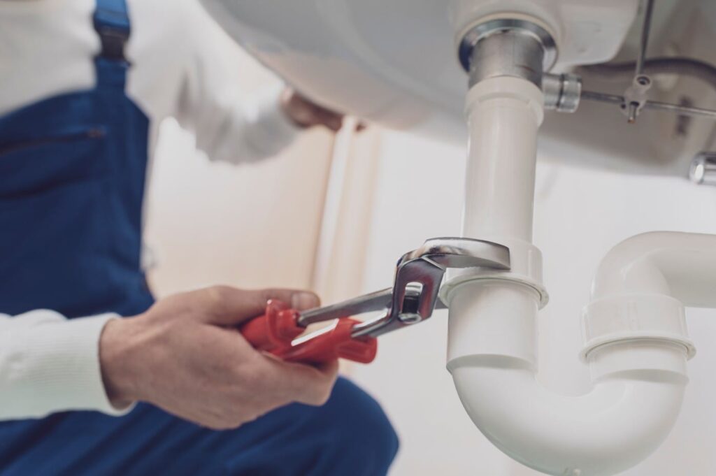 Plumber repairing a white drain pipe beneath a sink in Lebanon